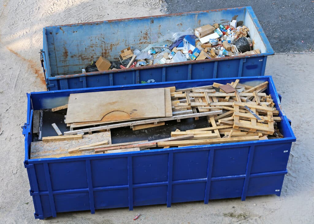 Bennes à Déchets Bleues : Bois, Cartons et Recyclage Vue de dessus de deux bennes à ordures bleues ; l'une remplie de déchets divers et cartons, l'autre de bois et palettes.