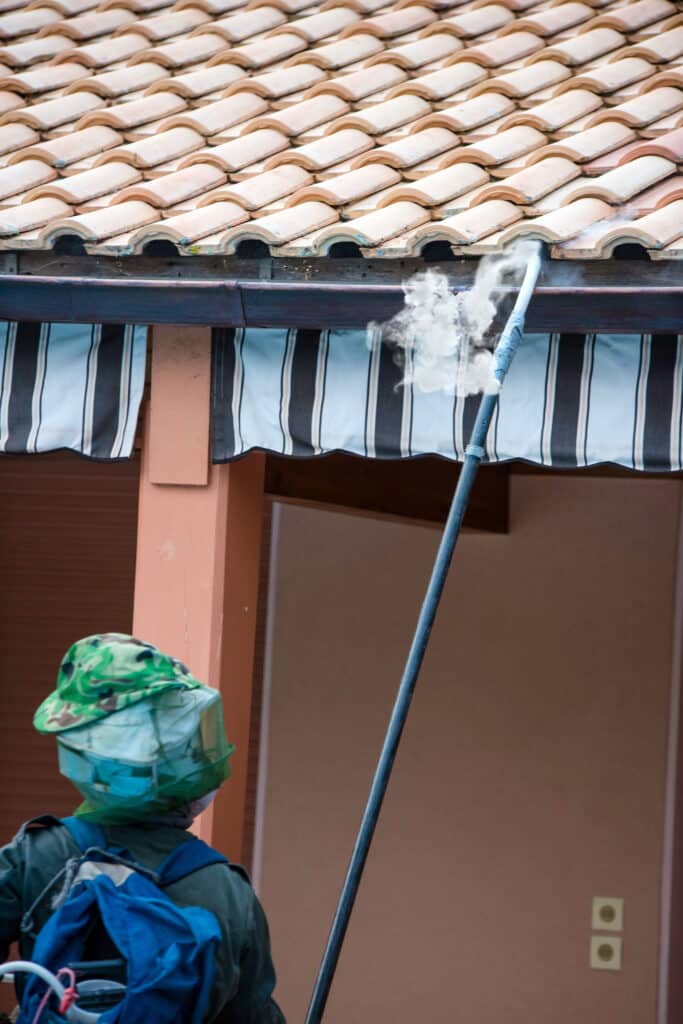 Nettoyage de gouttière à vapeur par apiculteur Apiculteur avec équipement de protection nettoie une gouttière de toit en tuiles romaines avec de la vapeur.