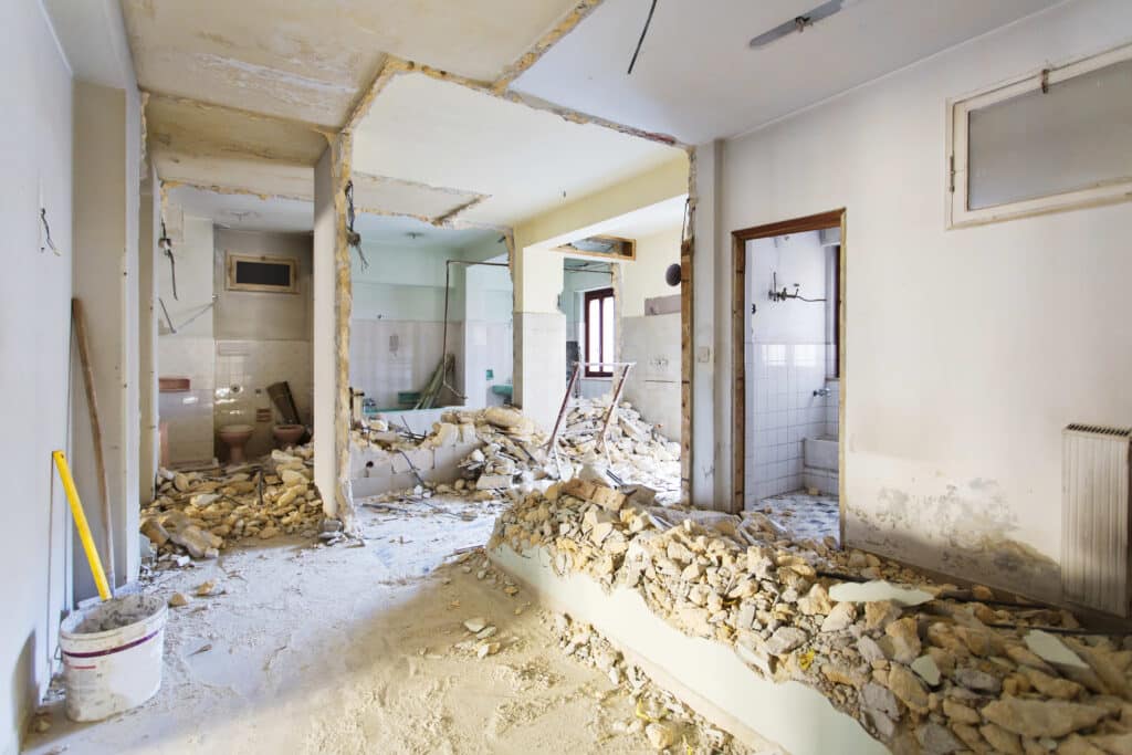 Rénovation appartement : murs cassés et démolition Intérieur d'un appartement en pleine rénovation, murs démolis révélant gravats, tuyauterie apparente et ancienne salle de bain carrelée.